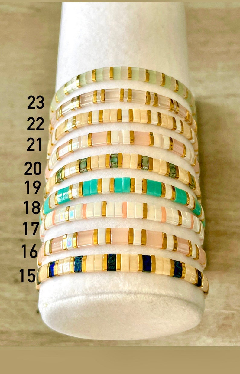 May include: A stack of 9 colorful beaded bracelets with gold accents. The bracelets are numbered 15 through 23.