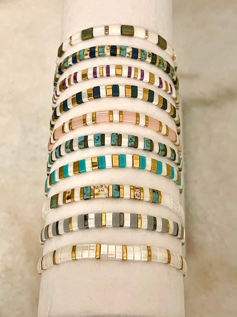 May include: A stack of colorful beaded bracelets with gold accents. The bracelets are made of various materials, including turquoise, white, and pink.