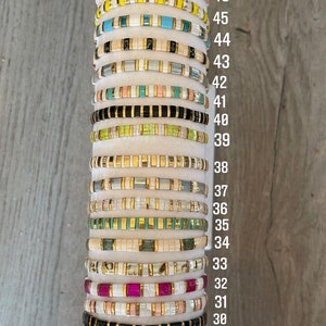 May include: A stack of 23 colorful beaded bracelets with gold accents. The bracelets are numbered from 28 to 50.