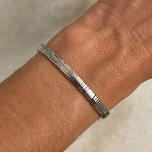 May include: A silver bracelet with a geometric design. The bracelet is made of multiple small, connected pieces.