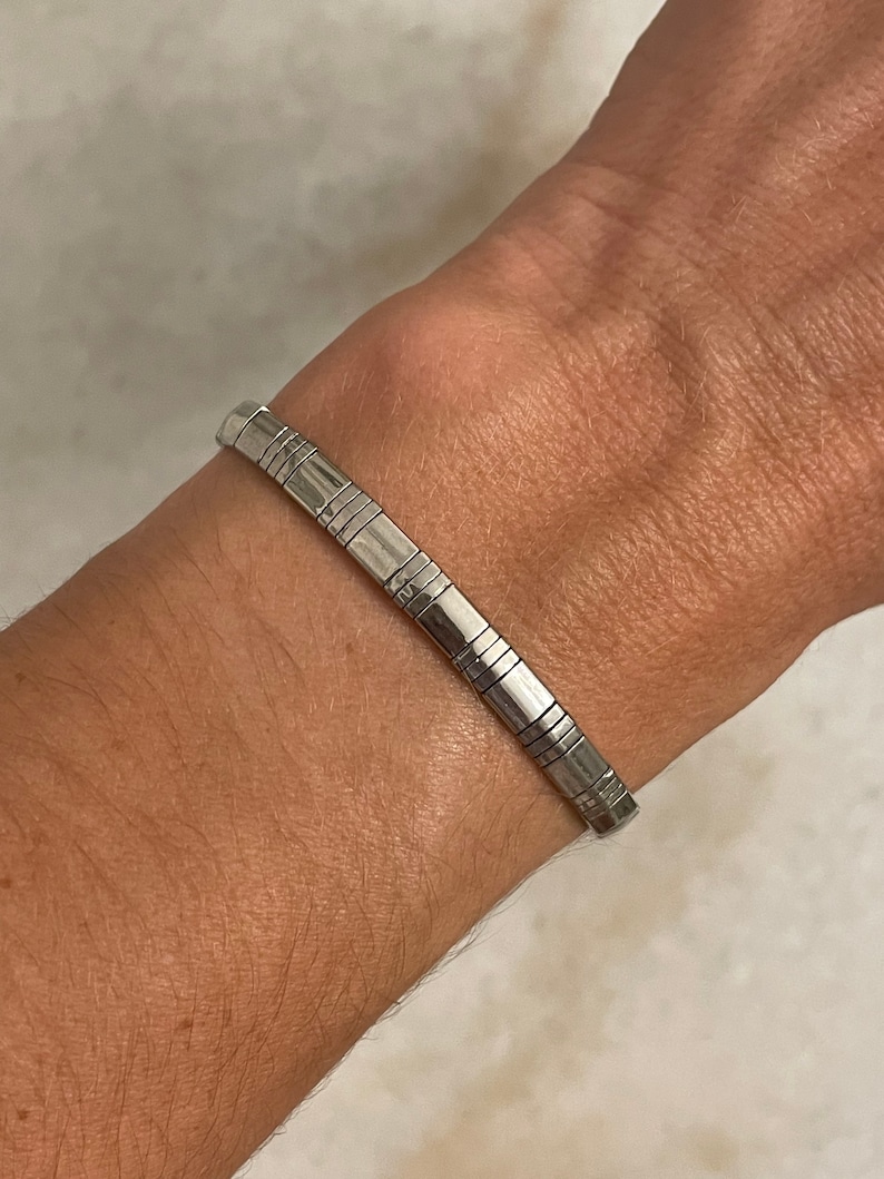 May include: A silver bracelet with a geometric design. The bracelet is made of multiple small, connected pieces.