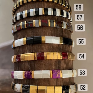 May include: A close-up of ten stacked bracelets with gold and colorful beads. The bracelets are numbered 51 through 59.
