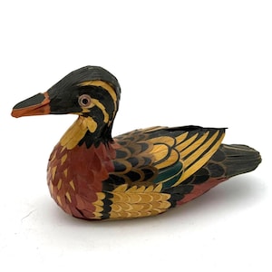 May include: A colorful wooden duck figurine with a black head and a red and orange beak. The duck's body features a mix of red, yellow, and green feathers. The figurine is a decorative item.