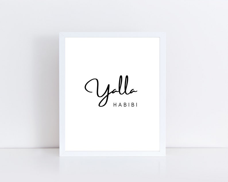 May include: White framed art print with the words "Yalla Habibi" in black script. The artwork is displayed on a white surface, creating a clean and minimalist aesthetic. The frame is a simple, modern design.
