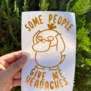 May include: Gold vinyl sticker with a cartoon duck and the text "Some people give me headaches".