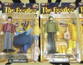 May include: Four Beatles Yellow Submarine action figures in original packaging. Each figure depicts a different character, with colourful outfits. The packaging displays the film's logo and artwork. The figures are in their original packaging.