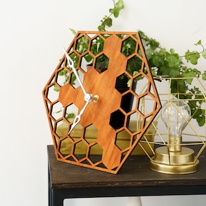 May include: A wooden clock with a honeycomb design. The clock is made of light brown wood and has silver hands. The clock is hanging on a wall.
