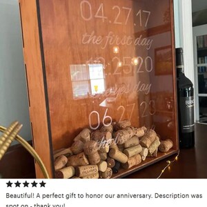 May include: A wooden box with a glass front, filled with wine corks. The glass is etched with the dates "04.27.17", "12.25.20", and "06.27.23" and the text "the first day" and "every day".