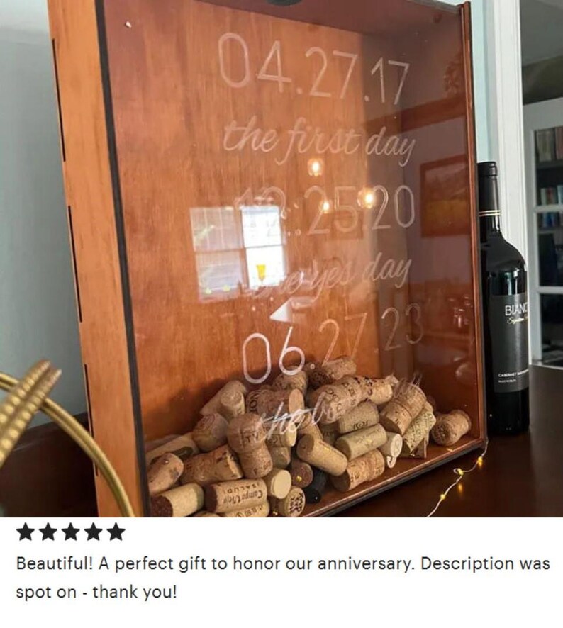 May include: A wooden box with a glass front, filled with wine corks. The glass is etched with the dates "04.27.17", "12.25.20", and "06.27.23" and the text "the first day" and "every day".
