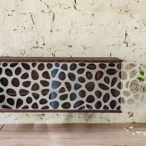 Puede incluir: Una estantería de pared de madera marrón oscuro con un patrón geométrico recortado en la parte delantera. El patrón está formado por muchos círculos y óvalos pequeños. La estantería está montada en una pared de ladrillo blanco.