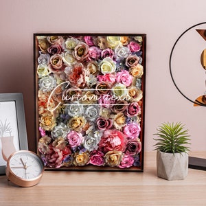 May include: A framed floral wall art piece with a variety of pink, white, and yellow roses. The frame is brown and the background is a light pink wall.