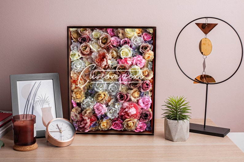May include: A framed floral wall art piece with a variety of pink, white, and yellow roses. The frame is brown and the background is a light pink wall.