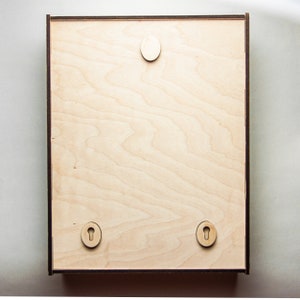 May include: A light wood frame with a smooth surface and three keyhole-shaped cutouts. The frame is ready to be hung on a wall.