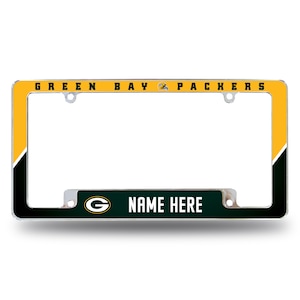 May include: Green Bay Packers license plate frame with a yellow and black background. The frame has a green and white "G" logo and the text "NAME HERE" on the bottom.