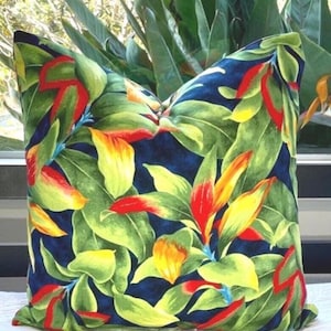 May include: Square throw pillow with a vibrant tropical floral pattern. The design features large green leaves, red and yellow flowers, and a dark blue background. The pillow is likely made of a soft fabric.