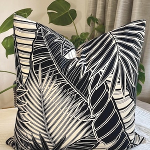 May include: Square throw pillow with a black and white tropical leaf pattern. The pillow features a bold design of large palm leaves and other foliage, creating a striking contrast. The pillow is likely made of a soft fabric.