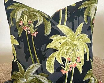 May include: Square throw pillow with a dark background and a repeating pattern of green palm trees with pink flowers. The pillow has a tropical theme and is likely used for home decor.