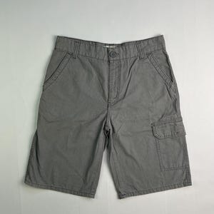 May include: Gray cargo shorts with multiple pockets and a button closure. The shorts have a classic design and are made of a durable fabric. The shorts are a neutral color, suitable for various outfits.