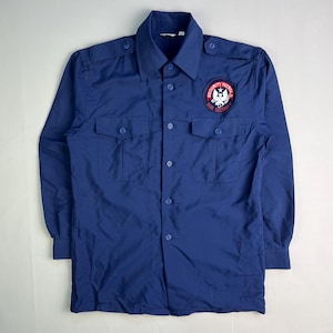 May include: A long-sleeved, navy blue button-up shirt with two chest pockets and shoulder epaulets. A circular patch on the left breast reads "SECURITY PATROL" in white lettering on a red background, with a white eagle emblem.