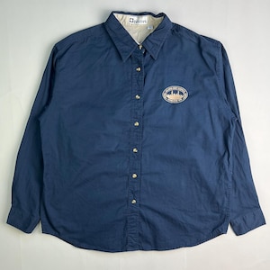 May include: A navy blue button-down shirt with long sleeves. The shirt features a beige collar and a small embroidered emblem on the chest with the text "ATLANTA WEST CARPETS". The shirt has gold-colored buttons.