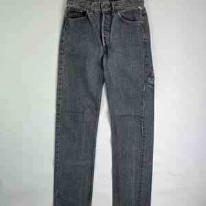 Puede incluir: Un par de vaqueros de mezclilla negros descoloridos. Los vaqueros tienen bragueta con botones, cinco bolsillos y un aspecto desgastado con desgaste visible en la tela. Los vaqueros son de corte recto.