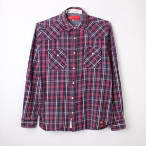 Może przedstawiać: Koszula w kratę z długim rękawem w kolorze czerwonym, granatowym i białym. Posiada dwie kieszenie na piersi, zapięcie na guziki i kołnierzyk. Koszula wykonana jest z tkaniny i ma klasyczny styl western.