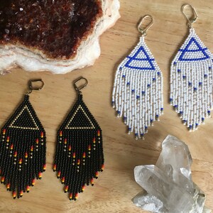 May include: Two pairs of beaded earrings. One pair is black with gold accents and red beads. The other pair is white with blue accents and gold beads.