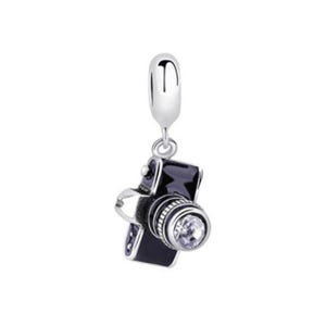 May include: A silver charm shaped like a vintage camera with black enamel detailing. The camera lens features a clear, round crystal. The charm has a silver loop for attaching to a bracelet or necklace.