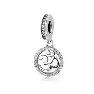 May include: Silver charm with a circular pendant featuring the Om symbol surrounded by clear cubic zirconia stones. The charm has a silver bead with clear cubic zirconia stones.
