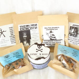 May include: A collection of six small food pouches and one round container with labels featuring horror movie themes including The Blair Witch Project, The Exorcist, A Nightmare on Elm Street, Jeepers Creepers, The Great Pumpkin, and Toxic Waste.