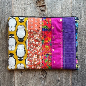 May include: A colorful patchwork zippered pouch with a repeating pattern of owls on one side. The pouch is made of various fabrics in shades of orange, pink, purple, and blue.