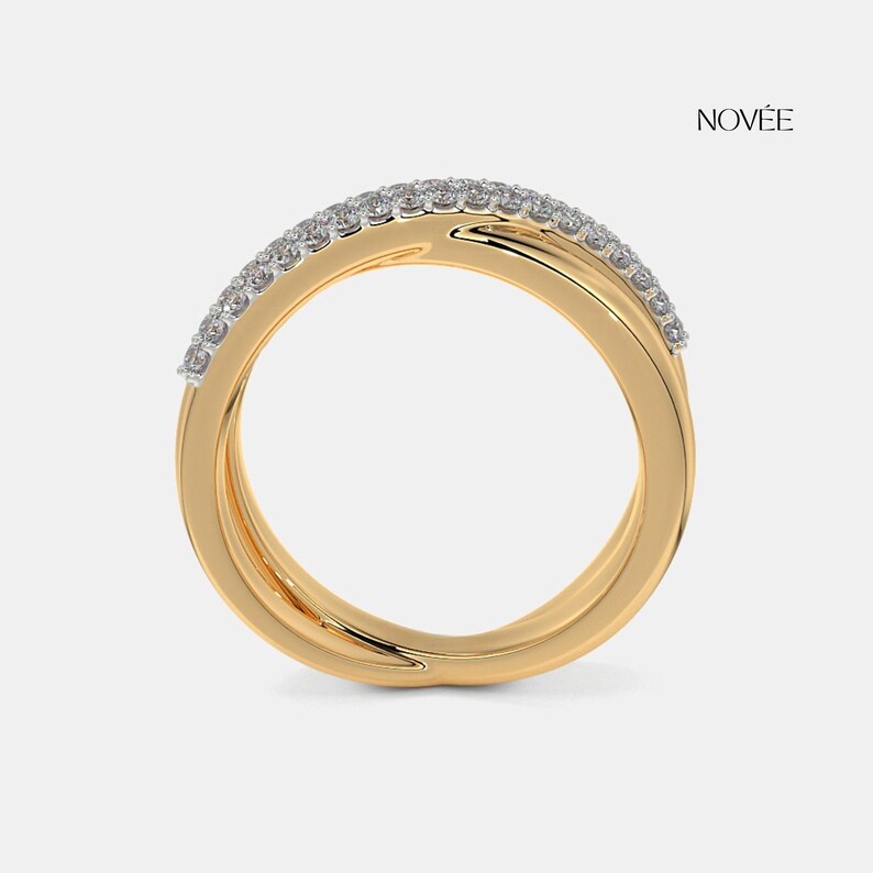 May include: A gold ring with a double band design. The top band is set with small, sparkling gemstones. The ring has a smooth, polished finish and is set against a neutral background. The word "NOVEE" is printed in black.