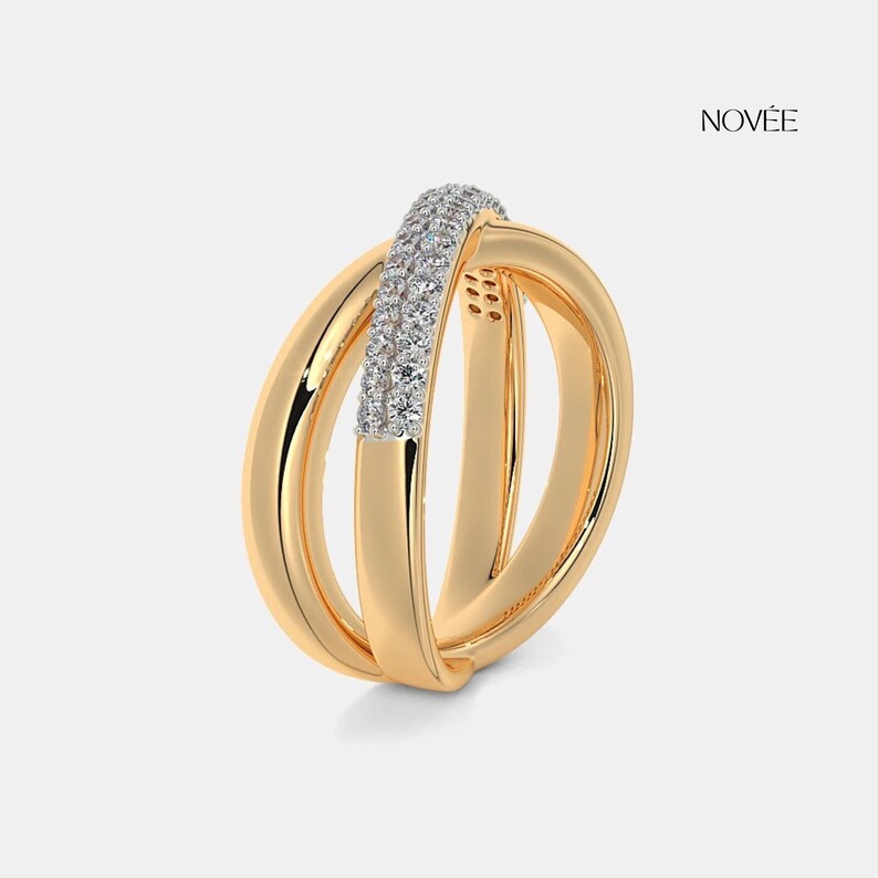 May include: A gold ring with a distinctive design. The ring has three interwoven bands, one of which is embellished with a row of small, sparkling stones. The word "NOVEE" is visible in the upper right corner.