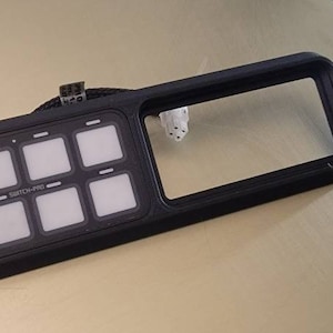 May include: A black electronic control panel with eight illuminated square buttons and the text "SWITCH-PRO". The panel has a rectangular frame with a large open area. A small white component is visible.