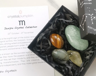 May include: A black box with a white and black label that says "crystalpumpkin" and "Scorpio Crystal Collection 23rd October - 21st November". The box contains four crystals: a brown tiger's eye, a green aquamarine, a green aventurine, and a clear citrine.