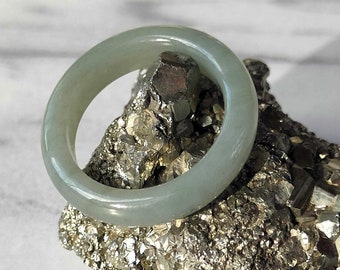 May include: A light green jade bangle ring resting on a bed of gray and silver pyrite crystals.