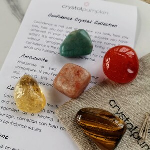 May include: A set of five crystals in a small pouch, labeled "Confidence Crystal Collection". The crystals are green aventurine, orange carnelian, yellow citrine, brown tiger's eye, and pink sunstone. The pouch is made of natural fabric and has the words "crystalpumpkin" printed on it.