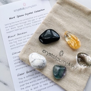 May include: A selection of crystals, such as black obsidian and citrine, presented on a beige linen pouch. A printed card with the text "Work Space Crystal Collection" is also visible.