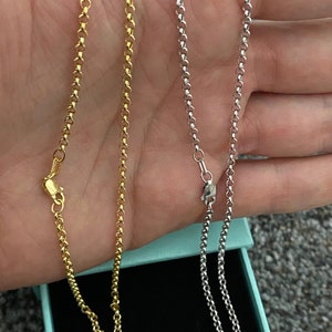 May include: Two gold and silver chain necklaces on a teal background. The chains are both the same style, but one is gold and the other is silver.