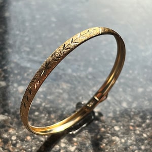 Puede incluir: Un brazalete de oro con un dise&ntilde;o texturizado. El brazalete est&aacute; hecho de un metal liso y brillante y tiene un dise&ntilde;o simple y elegante.