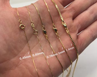 May include: A selection of gold-colored box chain necklaces in varying thicknesses, from 0.45mm to 1.4mm, displayed against a neutral background. Each chain is shown with its clasp and measurement clearly labeled, showcasing the different sizes available.
