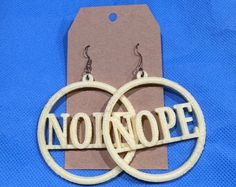 Puede incluir: Pendientes de aro color crema con la palabra "NOPE" en mayúsculas. Los pendientes cuelgan frente a una etiqueta marrón sobre un fondo azul. La palabra "NOPE" está recortada del aro.