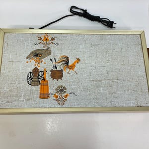 May include: Rectangular electric serving tray with a gold-colored frame and wooden handles. The tray features a light gray textured surface with a decorative print of a rooster, cooking utensils, and other kitchen-themed illustrations.