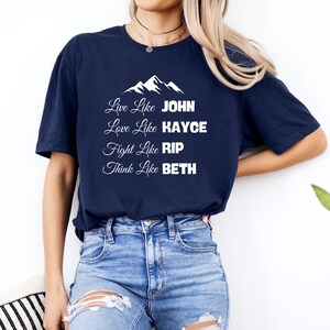 Könnte beinhalten: Marineblaues T-Shirt mit weißem Text und einem Bergmotiv. Der Text lautet "Live Like JOHN, Love Like KAYCE, Fight Like RIP, Think Like BETH". Das Shirt ist ein lässiger Stil.