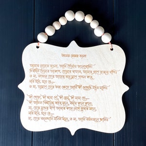 May include: A wooden plaque with a poem written in Bengali script. The poem is titled "Amar Sonar Bangla" and is about the beauty of Bangladesh. The plaque is decorated with a string of wooden beads.