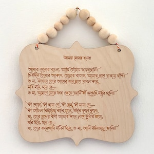 May include: A wooden plaque with a poem written in Bengali script. The poem is titled "Amar Sonar Bangla" and is about the beauty of Bangladesh. The plaque is hanging from a string of wooden beads.