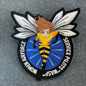 May include: A black and white embroidered patch with a yellow and black wasp with wings. The text around the wasp reads "W.A.S.P. Service Pilots...Women Airforce".