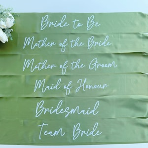May include: Six green satin sashes with white text. The sashes read: "Bride to Be", "Mother of the Bride", "Mother of the Groom", "Maid of Honour", "Bridesmaid", and "Team Bride".
