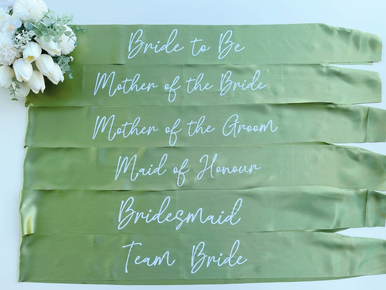 May include: Six green satin sashes with white text. The sashes read: "Bride to Be", "Mother of the Bride", "Mother of the Groom", "Maid of Honour", "Bridesmaid", and "Team Bride".