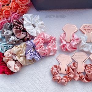 May include: A collection of 15 pink, white and blue satin scrunchies with the text "Will you help me? I'm the Knot!" on two of the scrunchies.